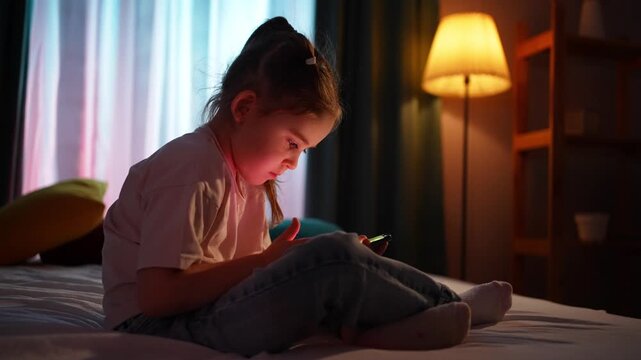 A lonely child sitting on a bed in a dark room in the evening, using a smartphone close up