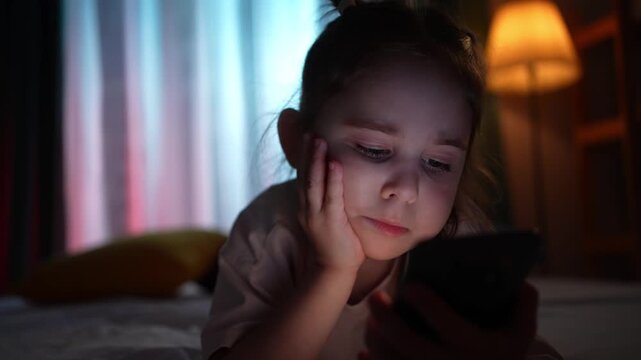 Close-up of a young girl face lying on a bed in the evening, holding a smartphone.