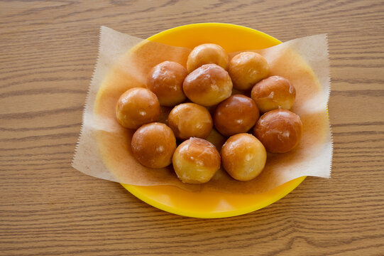 A dozen shiny, glazed donut holes on a sheet of wax paper on a plate.