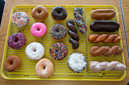 An assortment of glazed, iced, and plain donuts with sprinkles, coconut, or cinnamon spread out on a rack and ready to eat.