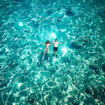 Couple swimming in crystal clear ocean water. Aerial view of people snorkeling in the sea.