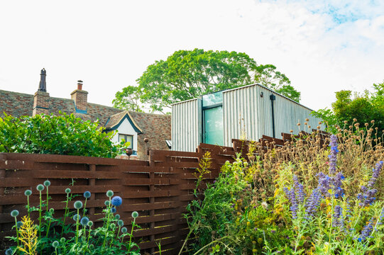 Unusual, modern metal building seen annexed on a traditional English cottage. Used as a home office and seen at a neighbours cottage garden in summertime.