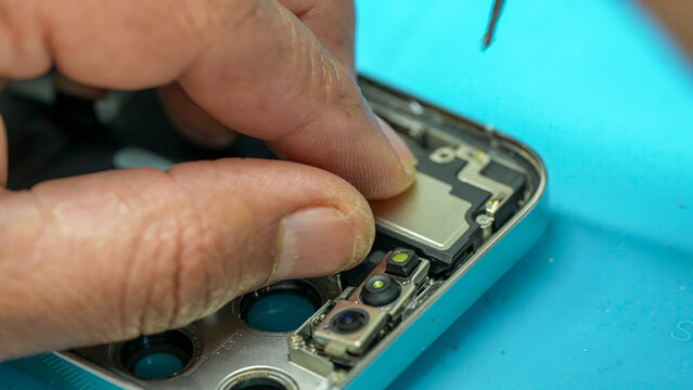 Repairing smartphone opened with visible internal components in electronics repair laboratory