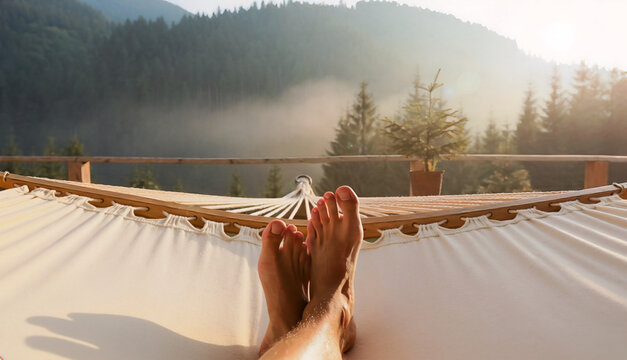 First person view of a person relaxing in a white fabric hammock on a wooden balcony during a lazy day, enjoying a peaceful morning scenery of misty pine forest mountains with warm sunlight.