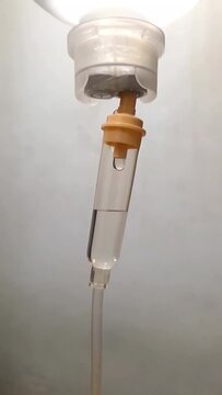 Close up of saline drip chamber with fluid drop in hospital room.