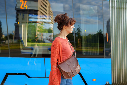 Thoughtful young woman standing beside modern blue tram after daily city commute