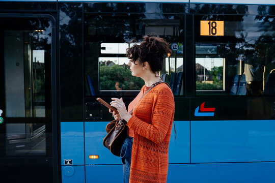 Attentive young female commuter waiting beside tram with smartphone in hand