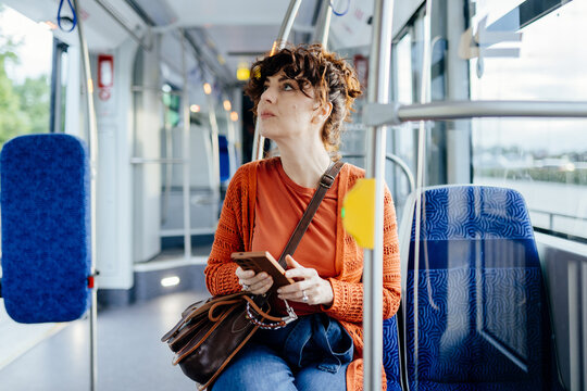 Attentive young woman holding smartphone inside modern tram during commute