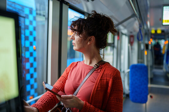 Thoughtful young woman watching city through tram window during daily commute