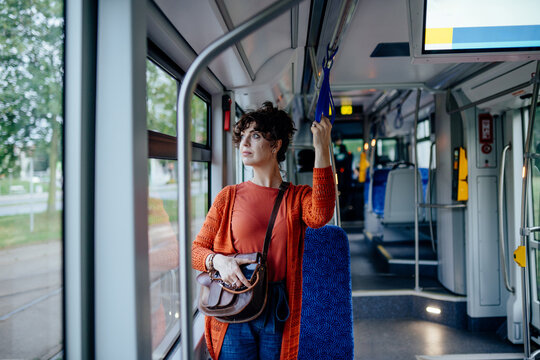 Attentive young female commuter holding strap and watching route inside modern tram