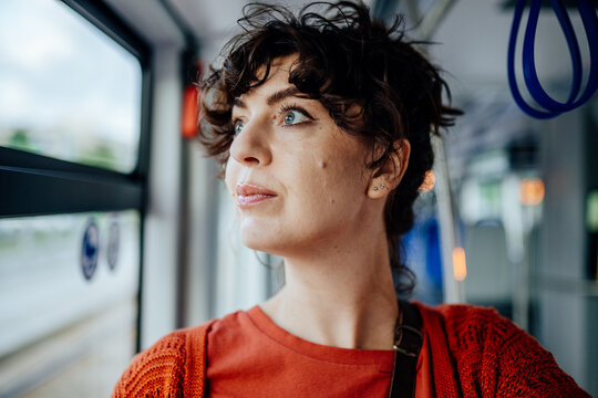 Thoughtful young female passenger looking through tram window in close portrait