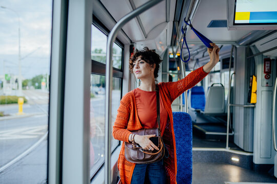 Confident young woman standing with smartphone during sustainable tram commute