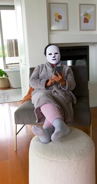 Vertical video: African American senior woman sitting at home with face mask tapping phone to rest