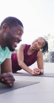 Vertical video: Diverse friends holding plank on rooftop mats, smiling and high-fiving after set