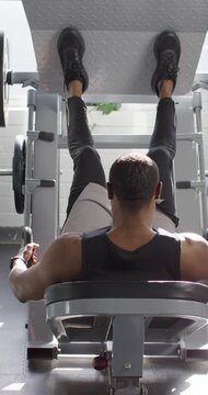 Vertical video: Bracing hands and feet, 30s man pressing and lowering footplate at gym for strength