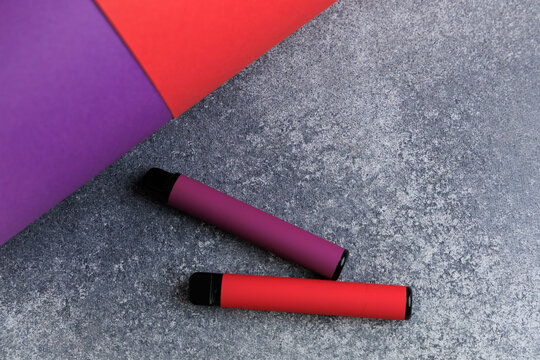 Electronic cigarettes are placed on a tabletop with a colorful background of red and purple paper in a minimal setting