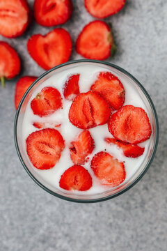 Fresh strawberries in a glass of creamy yogurt on a gray surface with sliced berries around