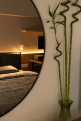 Fototapete Japandi A modern cozy bedroom reflected in a round mirror, featuring a bamboo plant, warm ambient lighting, soft bedding and minimalist wood accents for a calm, inviting interior atmosphere.  © Manual Mood