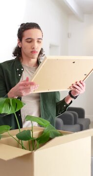 Vertical video: African American man standing at counter unpacking box, inspecting frame and plant
