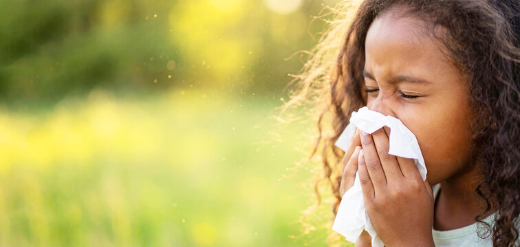 Dark-skinned little girl with the flu is blowing her nose and appears unwell with space for text. The child may be suffering from sinusitis, allergies, or other symptoms, holding a tissue