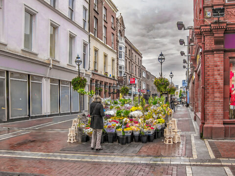 A lone woman on a wet street in London looking at flowers for sale but nobody is around, brick road, overcast, sense of isolation
