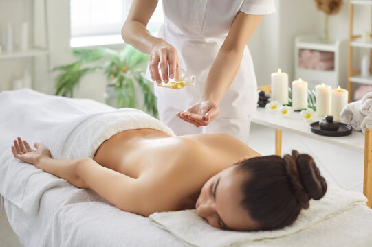 Massage spa therapy with oil and candles. A therapist masseuse pours warm oil before a back treatment as the client rests on a soft table in calm beauty studio. Relaxation, body care and wellness.