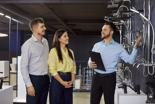 Salesperson guides couple on faucet in showroom. Friendly consultation in a modern plumbing store, helping the buyer compare finishes and prices for choice. Clear purchase choice in retail.