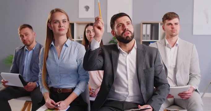 Group of young people employees sitting in office on a meeting and listening a business speaker. Man raising hand to answer a question during conference or business training. 4k video.