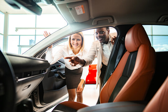 Diverse people looking at car interior in dealership with saleswoman pointing