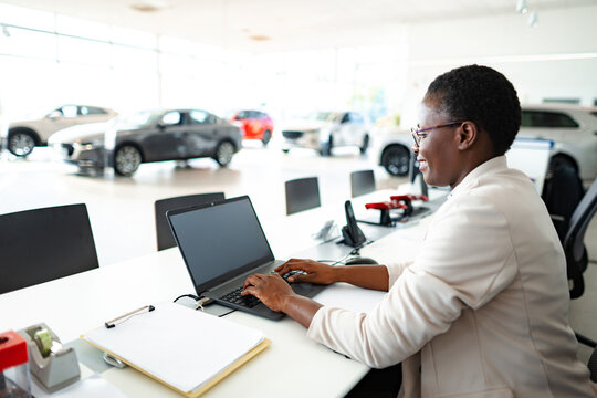 Smiling businesswoman working on laptop at desk in modern car showroom