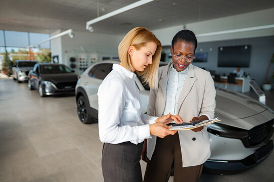 Two business women reviewing paperwork for a vehicle purchase in a car showroom