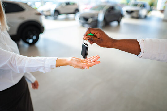 Car salesperson handing over new car key to happy customer at dealership showroom