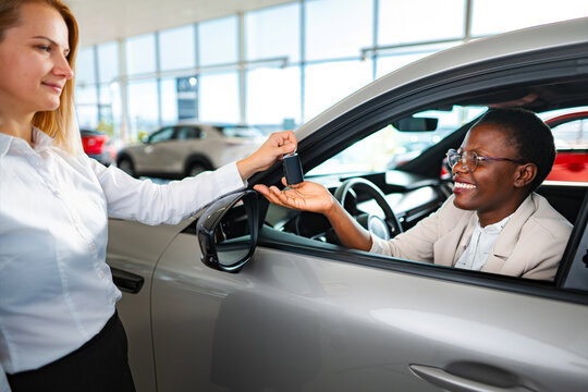 Saleswoman giving vehicle keys to smiling customer inside car dealership