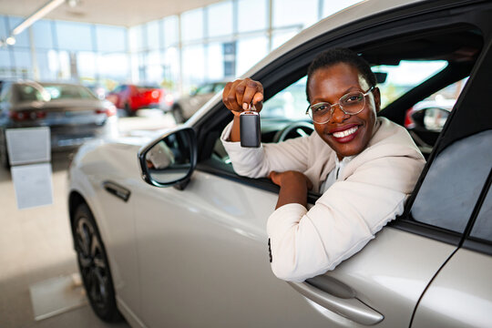 Woman in new car smiling holding key in a dealership