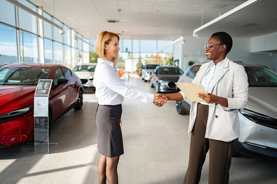 Car salesperson shaking hands with customer after buying new vehicle at dealership