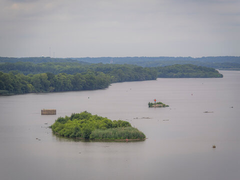 Wide aerial view of small wooded islands and a navigation marker in a large expansive river surrounded by green forests