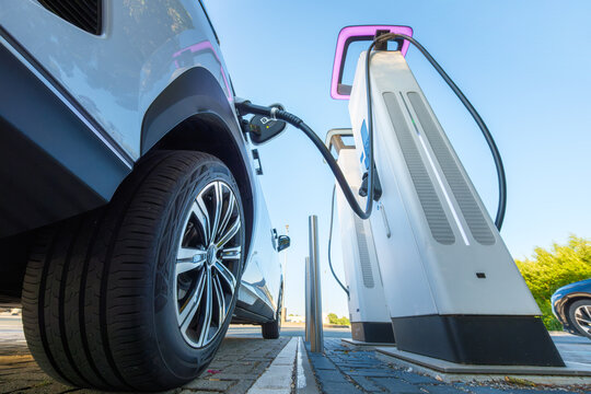 Electric car charging at a outdoor public charging station. Close up of EV charger cable connected to modern electric vehicle.