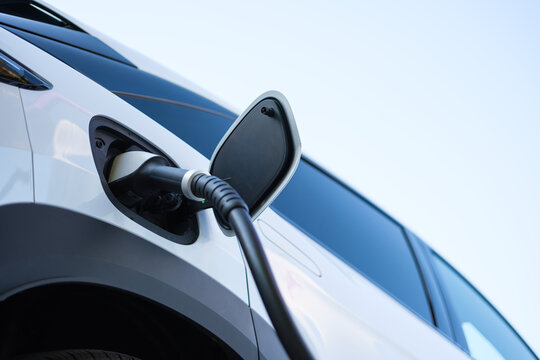 Electric car charging at a outdoor public charging station. Close up of EV charger cable connected to modern electric vehicle.