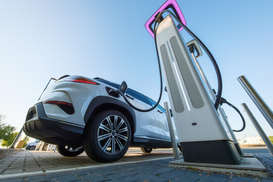 Electric car charging at a outdoor public charging station. Close up of EV charger cable connected to modern electric vehicle.