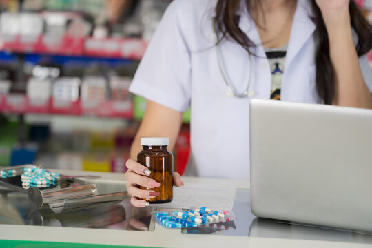 Pharmacist holding a bottle of pills with a laptop and medication on the counter