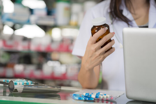 Pharmacist holding medication bottle near laptop and pills on counter