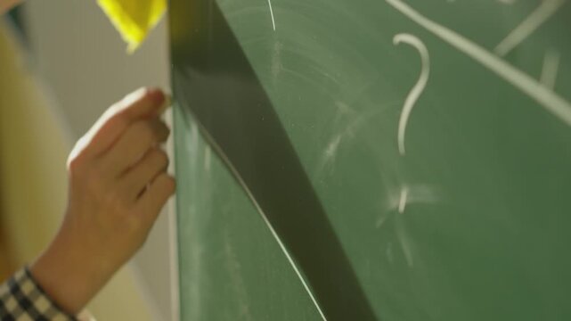A person&rsquo;s hand wipes away chalk dust from a blackboard, partially erasing a large question mark. The image symbolizes inquiry, problem solving, and the pursuit of knowledge in an academic setting