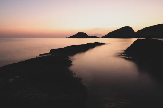 A beautiful sunrise over the dramatic shoreline of Mandrakia on the Greek island Milos. Calm water and vibrant colors. 