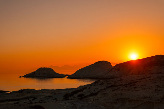 A beautiful sunrise over the dramatic shoreline of Mandrakia on the Greek island Milos. Calm water and vibrant colors. 