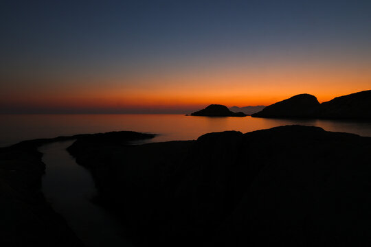 A beautiful sunrise over the dramatic shoreline of Mandrakia on the Greek island Milos. Calm water and vibrant colors. 