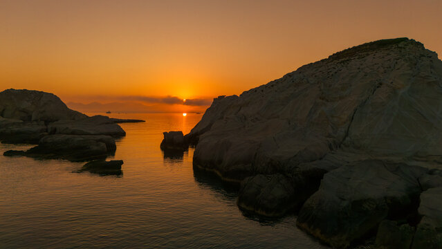 Sunrise over Mandrakia near Sarakiniko Beach on Milos Island, Greece, illuminating the volcanic coastline and calm Aegean Sea with warm golden light, vibrant colors,  in a Mediterranean atmosphere.