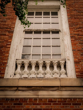 Low angle view of a tall vintage multi pane window with a white balustrade on an old red brick building facade