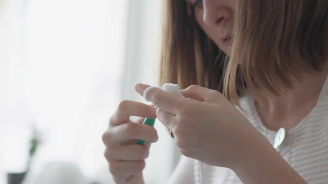 A woman applies first aid to her injured finger, using a cotton pad and antiseptic, emphasizing health and safety. The scene highlights modern self care and home healthcare routines