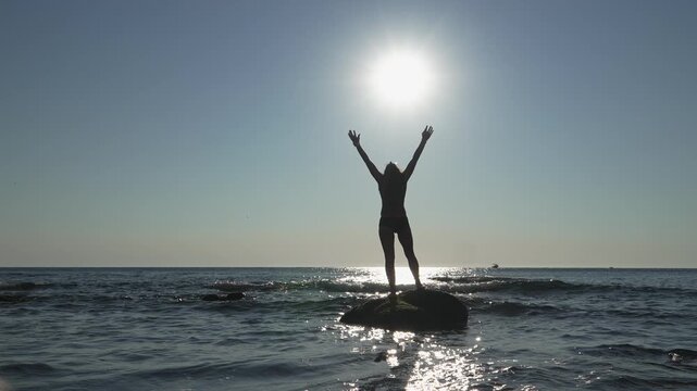 A lone figure stretches upward on a rocky outcrop surrounded by tranquil water, basking in the golden sunlight. The serene seascape evokes freedom, mindfulness, and connection with nature