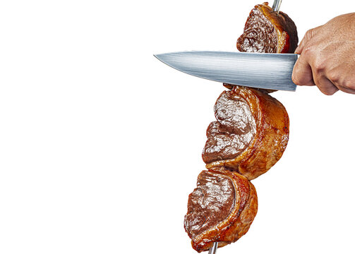 Close-up of a hand slicing juicy roasted picanha beef on a skewer with a knife